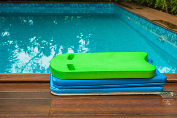Pile of colorful swimming foam board put on edge of swimming pool for kids. (Selective focus)
