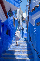 Woman with white djellaba walking the blue streets of Chefchaouen, Morocco.