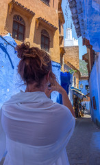 Tourist woman with white djellaba taking a photo in the blue streets of Chefchaouen, Morocco.