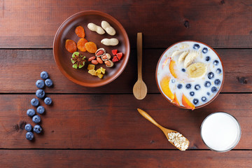 Oatmeal with milk and fruits, blueberries on wooden boards, vegetarian food, healthy porridge with banana and peach slices, breakfast in vintage style