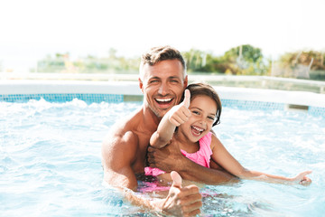 Photo of happy family father with daughter smiling, while swimming in pool outdoor during summer...