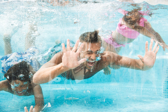 Photo of happy family father with children diving and swimming under water in pool, during summer vacation