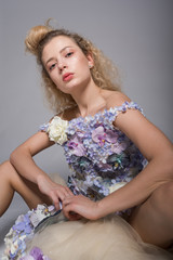 Beautiful young woman is dressed in a avant garde long dress from flowers. Fashion Studio Portrait
