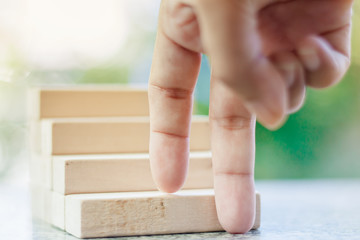 Fingers moving step up the wooden toy staircase against blurred natural green background for step to goal success concept