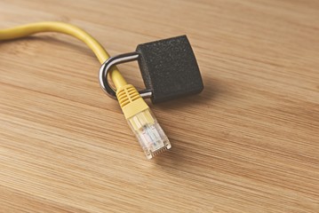 A cyber security concept image consisting of an Ethernet cable, padlock and a wooden background.  