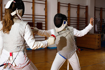 Two female fencers  exercising movements in duel at fencing room