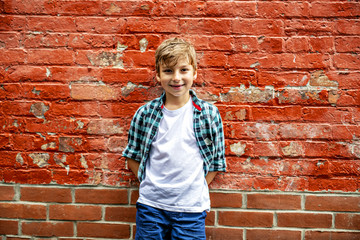 Adorable cute boy staing near a red brick wall