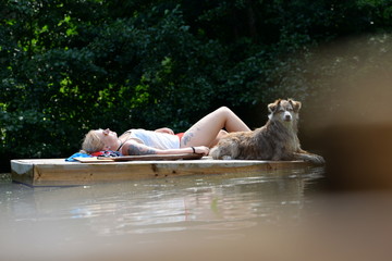 watching you, cute shepherd dog lying upon a wooden raft in a lake next to a pretty girl
