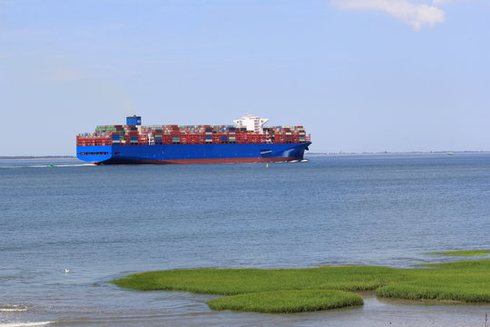 a large container ship navigates through the westerschelde sea towards antwerp along green grass humps in the salt marsh 