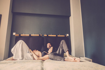 happy caucasian couple of people with pregnant woman and new dad laying on the bed at home and...