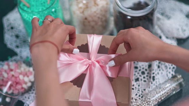 Girl fixes a bow on gift box with cookies.
