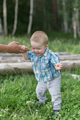 Baby boy holds his father's hand on the village meadow. Father is teaching his son how to walk.