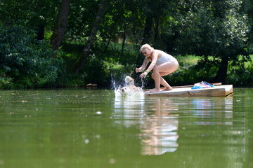 ab ins Wasser! Junge blonde Frau schubst Hund vom Floß ins Wasser
