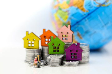 Miniature people: standing on coins stack with house, money saving growth. Retirement, emergency plan and Financial Concept.