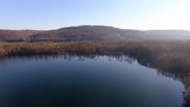 A flight over a natural lake in a forest in fall, before the sunset.