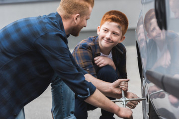 ginger hair father and son changing tire in car with wheel wrench