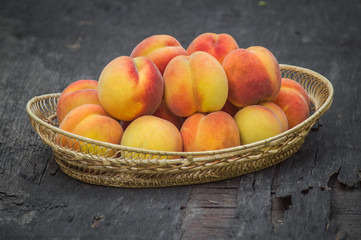 Fresh peaches in wicker basket on dark wood background