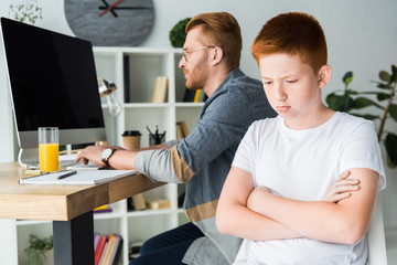 Obraz premium father using computer and sad son looking down at home