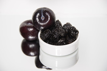 Prunes and plums on white background with reflection