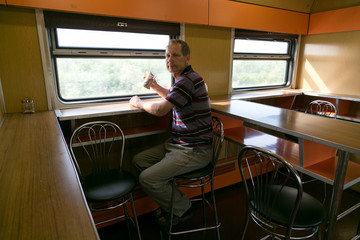 A man is riding in a train restauran.  A man 40 - 50 years old is drinking tea in a long-distance train.