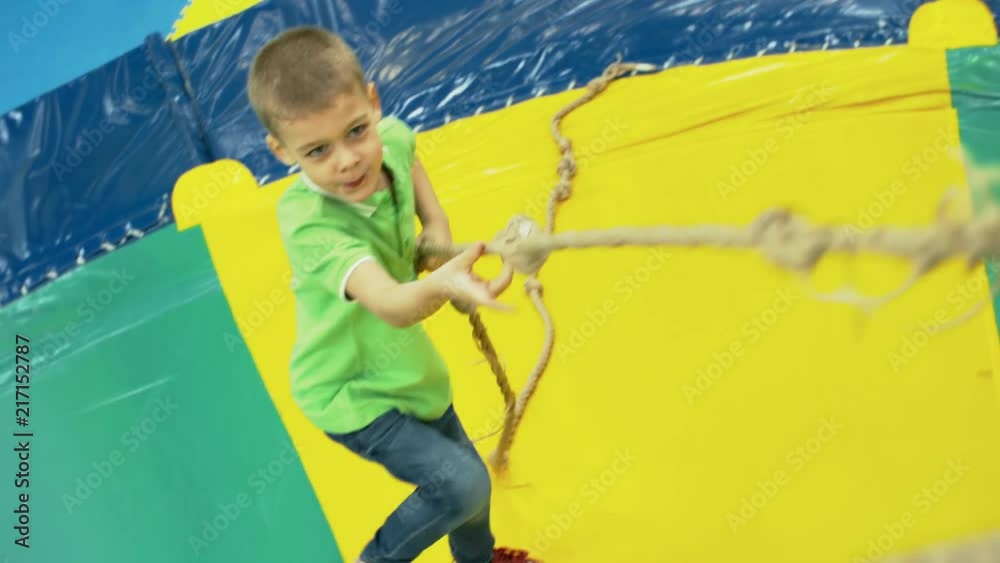 Wall mural front view of playful little boy climbing inflatable structure in children play center using climbin