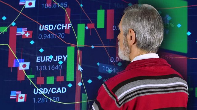 An elderly man looks at a currency market in the background