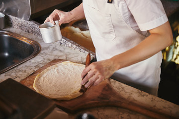 cropped shot of chef making pizza at restaurant kitchen