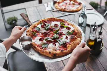 cropped shot of woman carrying plate with tasty pizza to serve on table at restaurant