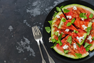 A fresh watermelon grill with feta cheese and greens on a rustic dark gray background. View from above, flat lay.