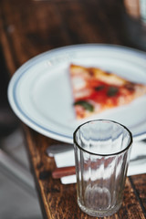 close-up shot of drinking glass with blurred slice of pizza on plate