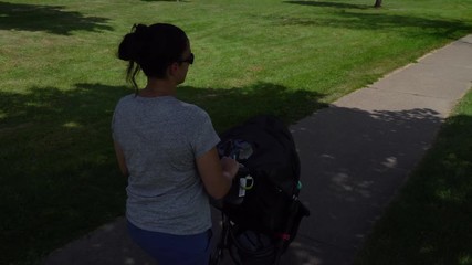Young healthy mother walking baby stroller through park on a beautiful summer day. Exercise and outdoor activity important for postpartum treatment and child stimulation. 4K stock video