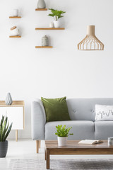Simple shelves with vases on a white wall and wooden, scandinavian furniture in a bright living room interior with gray decor