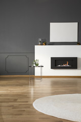 Mockup of white empty poster above fireplace in grey flat interior with round rug. Real photo