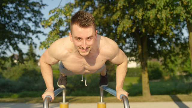 PORTRAIT: Muscular man does push ups on parallel bars in awesome outdoor gym.