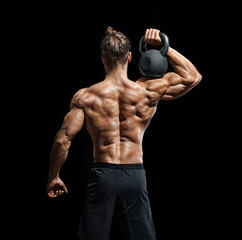 Fototapeta na wymiar Young bodybuilder doing exercise with kettlebell. Rear view of muscular male with perfect physique on black background. Strength and motivation.