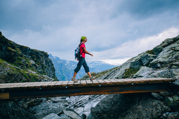 Young sportive woman tourist hiker on rocky trail crossing a wooden bridge over Norway scandinavian landscape background. Adventure, travel, leave your comfort zone concept.
