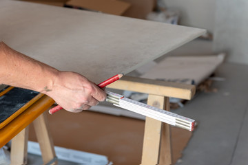The man measures the floor tiles to cut them using a tile cutting machine