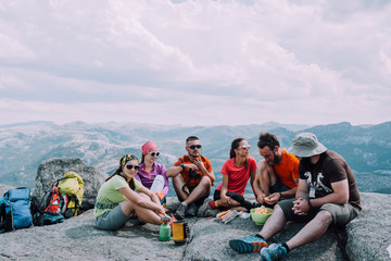 People friendship hangout traveling destination camping concept. Group of six hungry hikers travelers in sportswear relaxing and having snacks after hiking at top of mountain. - obrazy, fototapety, plakaty