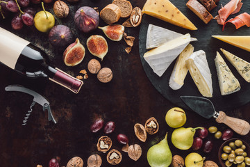 flat lay with assorted cheese, bottle of wine and fruits on dark surface