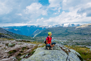 Fototapeta premium Travel in Norway, woman hiker with backpack sitting on big stone and enjoying scandinavian summer view.