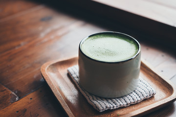 A cup of hot matcha latte on wooden floor