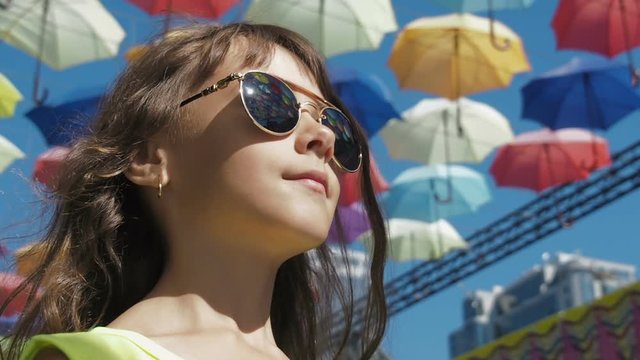 The girl dreams. A little girl in sunglasses against the background of colored umbrellas.
