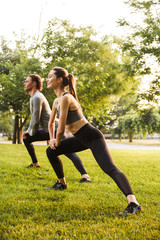 Sport loving couple friends in park outdoors make stretching exercises.