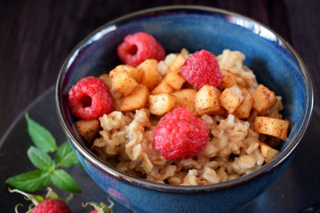 Porridge with apples, raspberries and honey topped with mint. Healthy breakfast meal