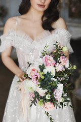 Sensual and sexy brunette model girl with bright make-up, in fashionable lace dress with naked shoulders and with bouquet of flowers in her hands posing at luxury vintage interior