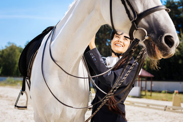 Long braid. Beautiful dark-haired female rider with long braid taking care of her white racing horse