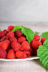  Red fresh raspberries on white rustic wood background. Plate with natural ripe organic berries with green leaves.flat lay with copy space