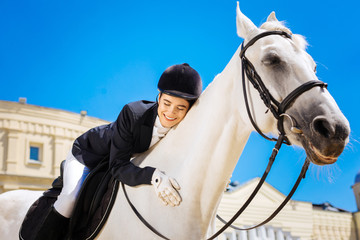 Great love. Smiling beaming professional female rider loving her white racing horse greatly