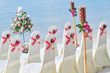 Back side of white cover wedding chairs with red pink organza sash and cone of roses petal