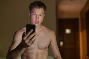 Fototapeta premium Shirtless Man Using Mobile Phone At Night In Bed